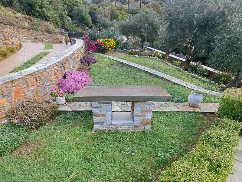 Κήπος με καμπύλο πέτρινο τοιχίο, πλακόστρωτα μονοπάτια και πέτρινο τραπέζι
