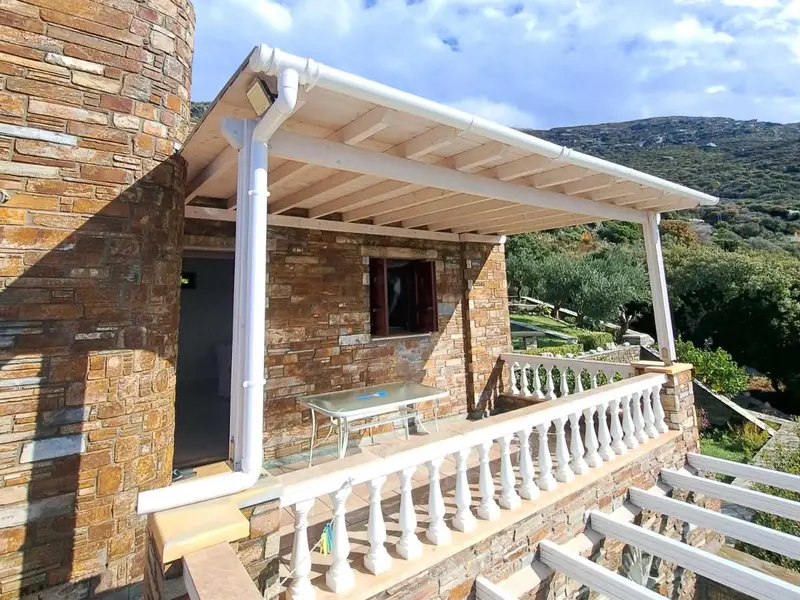 Ξύλινη στέγη πάνω από βεράντα με λευκή μπαλουστράδα, σε πέτρινο σπίτι με στρογγυλό πύργο